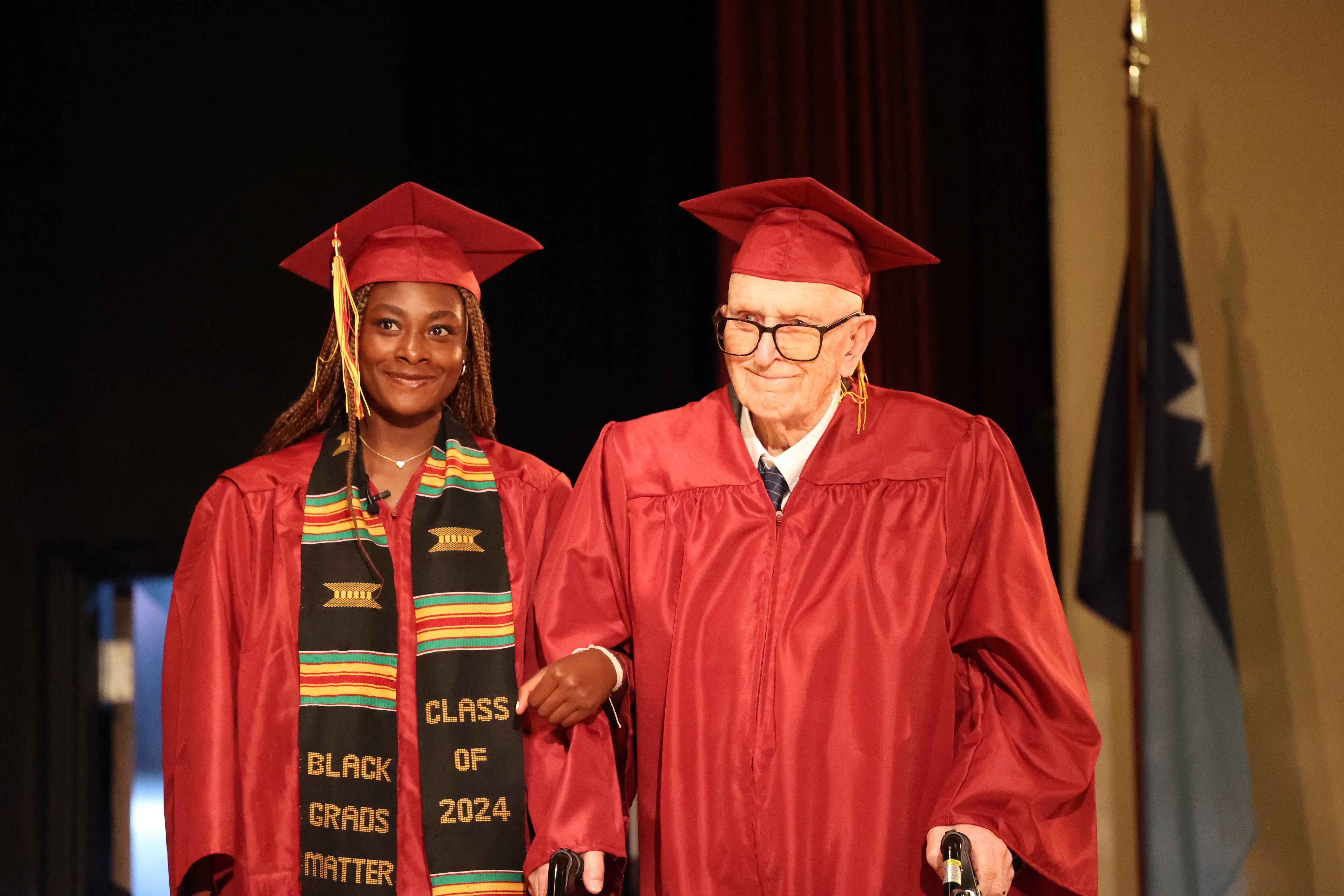 Harlan Olson, 101, walks across the stage at Denfeld High School with senior Grace Nonnemacher